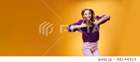 Optimistic and joyful bright ginger girl jumping happily and cheerful having fun showing thumbs up in like and approval giving positive feedback of super cool idea or concept over orange wall 98144914