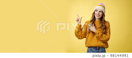 Curious attractive young 20s woman intrigued what hiding left pointing sideways looking interested smiling excited peeking cool fantastic promotion, standing joyfully yellow background 98144991
