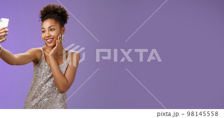 Popular stylish african-american female blogger take selfie partying night club extend arm holding smartphone posing looking phone display gladly grinning standing blue background in elegant dress Popular stylish african-american female blogger take selfie partying night club extend arm holding smartphone posing looking phone display gladly grinning standing blue background in elegant dress 98145558