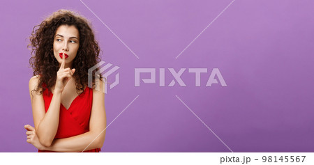 Keep it secret babe. Confident and tricky caucasian female with curly hairstyle in red elegant dress shushing looking left curious wanting tell secret showing shh gesture with index finger over mouth Keep it secret babe. Confident and tricky caucasian female with curly hairstyle in red elegant dress shushing looking left curious wanting tell secret showing shh gesture with index finger over mouth 98145567