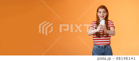 Amused excited redhead female record video thrilled see famous person, smiling amazed hold smartphone taking picture, tourist adore trip shooting everything during summer journey, orange background Amused excited redhead female record video thrilled see famous person, smiling amazed hold smartphone taking picture, tourist adore trip shooting everything during summer journey, orange background 98146141