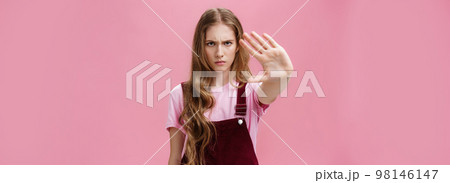Woman protest against testing products on animals. Serious-looking confident young girl with long wavy hair frowning looking sctrict at camera pulling palm towards camera in prohibition and no gesture Woman protest against testing products on animals. Serious-looking confident young girl with long wavy hair frowning looking sctrict at camera pulling palm towards camera in prohibition and no gesture 98146147