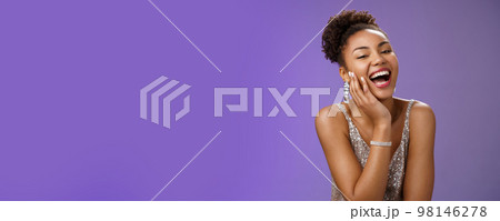 Cheerful attractive happy african american woman in elegant silver light dress laughing flirty giggling enjoying boyfriend sense humour jokes touch cheek coquettish gaze amused, blue background 98146278