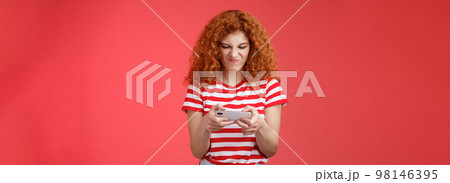 Daring enthusiastic addicted geeky good-looking redhead curly girl hate losing battles smartphone game wrinkle nose grimacing upset eager win tap fast telephone screen look display, red background Daring enthusiastic addicted geeky good-looking redhead curly girl hate losing battles smartphone game wrinkle nose grimacing upset eager win tap fast telephone screen look display, red background 98146395