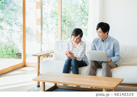 リビングでスマホとパソコンを見る若い夫婦 98148329