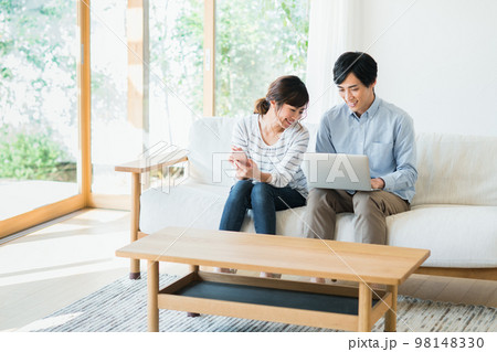 リビングでスマホとパソコンを見る若い夫婦 98148330