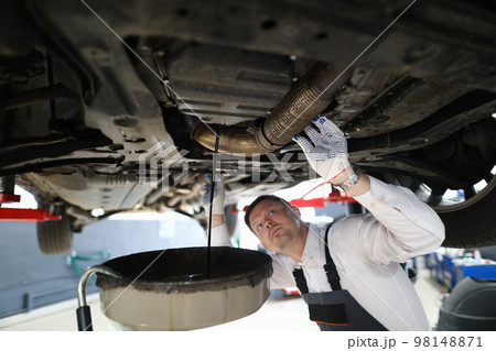 Handsome auto mechanic checks undercarriage of car at service station 98148871
