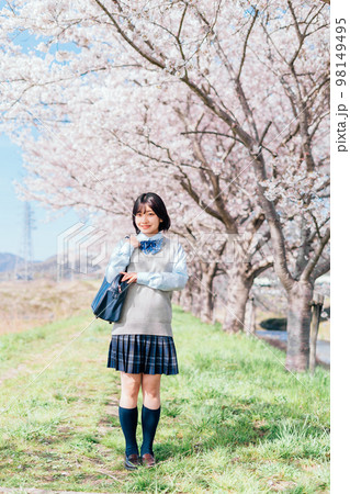 桜の咲いた河川敷を通学する女子高生 98149495