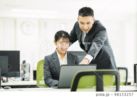 同僚とパソコンで仕事をするビジネスパーソン 98153257