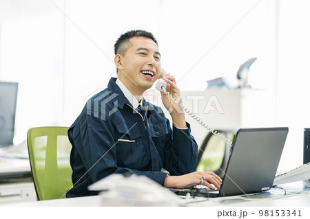 オフィスで電話対応する作業服の男性 98153341