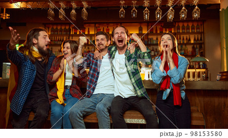 Group of young people, friends, emotionally watching match at pub. Fans cheering up favourite sport team. Winning game. Success 98153580
