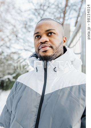 Young African man in casual white and gray clothes, sport jacket on street. Winter season urban portrait with snow. Lifestyle, city life concept. Close up Young African man in casual white and gray clothes, sport jacket on street. Winter season urban portrait with snow. Lifestyle, city life concept. Close up 98154014