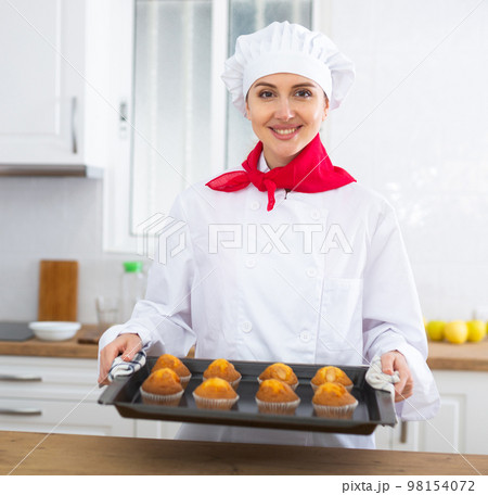 Smiling female chef in white uniform baking sweet cupcakes 98154072