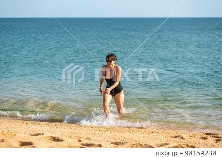 Woman sea swimsuit sand. The girl comes out of the sea in a black swimsuit after swimming. Alone on the beach on a sunny day. Woman sea swimsuit sand. The girl comes out of the sea in a black swimsuit after swimming. Alone on the beach on a sunny day. 98154238