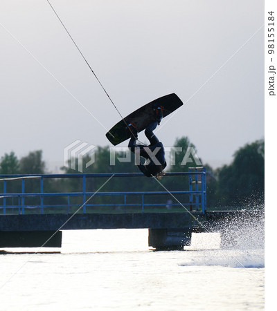 Wakeboarder making tricks while wakeboarding on lake. Young man surfer having fun wakesurfing in the cable park. Water sport, outdoor activity concept. 98155184