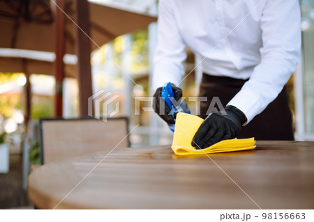 Waiter Cleaning The Table With Disinfectant Spray In A Restaurant