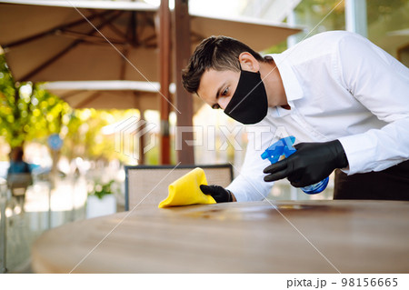 Disinfecting to prevent COVID-19. Waiter cleaning the table with Disinfectant Spray in a restaurant. 98156665