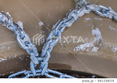 Wheel in the snow with safety and anti-skid chains. Loader or tractor with chains on wheels close-up. Driving safety in winter conditions 98158659