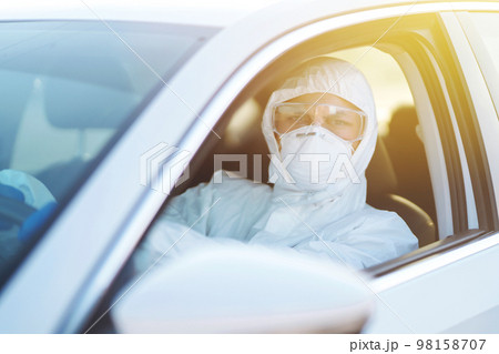 Man in Hazmat suit, protective gloves and goggles driving car during an epidemic in quarantine city. 98158707