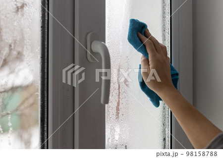 A womans hand wipes the condensate from the window glass with a towel. A womans hand wipes the condensate from the window glass with a towel. 98158788