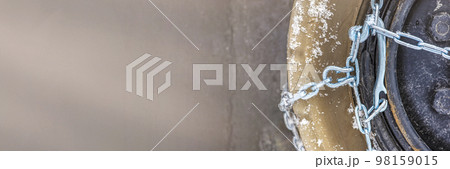 Wheel in the snow with safety and anti-skid chains. Loader or tractor with chains on wheels close-up. Driving safety in winter conditions Wheel in the snow with safety and anti-skid chains. Loader or tractor with chains on wheels close-up. Driving safety in winter conditions 98159015