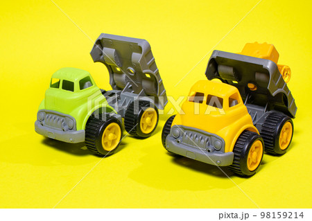 Two plastic trucks on a yellow background. Toys for a boy toy store. Two plastic trucks on a yellow background. Toys for a boy toy store. 98159214