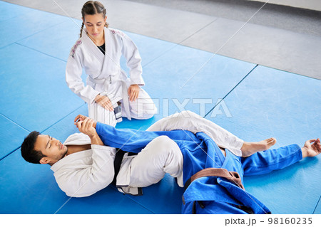 Karate, personal trainer and self defense training in the dojo for physical protection or health and safety. Black belt sensei man teaching woman to defend herself in a fight or combat at the gym 98160235