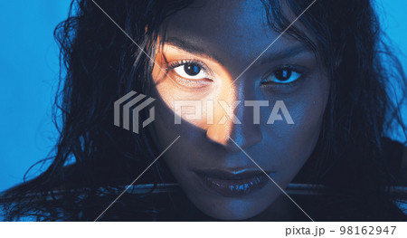 Beauty, cosmetics and portrait of a model with a light reflection on her face in the studio. Spotlight, skincare and young woman from Puerto Rico with natural skin isolated by a blue background. 98162947