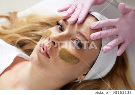 Cosmetologist applying a clay mask to the face of beautiful woman. Spa treatment and face care in the beauty salon 98163132