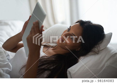 Browsing in bed. a beautiful young woman relaxing in bed with her tablet. 98164083