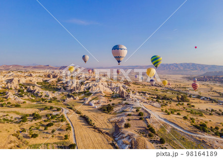 Colorful hot air balloons flying over at fairy chimneys valley in Nevsehir, Goreme, Cappadocia Turkey. Spectacular panoramic drone view of the underground city and ballooning tourism. High quality 98164189