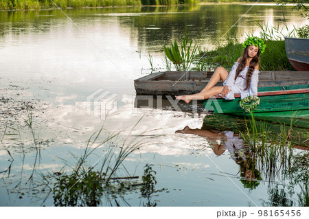 Young woman with flower wreath on her head, relaxing on boat on river at sunset. Concept of female beauty, rest in the village Young woman with flower wreath on her head, relaxing on boat on river at sunset. Concept of female beauty, rest in the village 98165456