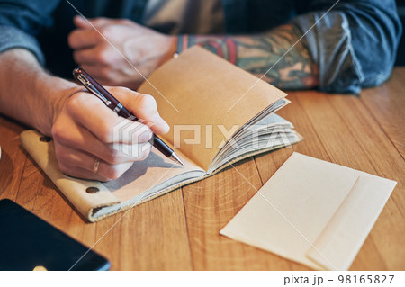 Man hand with pen writing on notebook on a wooden table. Close-up Man hand with pen writing on notebook on a wooden table. Close-up 98165827
