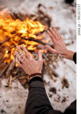 Traveller warming hands by the campfire outdoors. Camping detail, travel lifestyle photo. 98167237