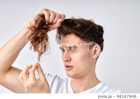confused guy looking at split hair ends, want to cut isolated over light gray background confused guy looking at split hair ends, want to cut isolated over light gray background 98167846