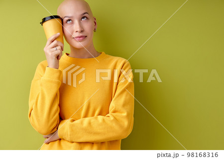 Portrait of thoughtful bald female holding cup of coffee in hands looking at side Portrait of thoughtful bald female holding cup of coffee in hands looking at side 98168316