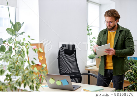 Young man office worker concentrated on work, writing planning, standing behind desk Young man office worker concentrated on work, writing planning, standing behind desk 98168376