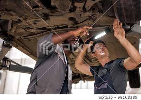 Young auto mechanics working on undercarriage of car diligence attention inspection Young auto mechanics working on undercarriage of car diligence attention inspection 98168389
