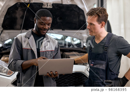Handsome diverse mechanics in uniform examining car while working in workshop service Handsome diverse mechanics in uniform examining car while working in workshop service 98168395