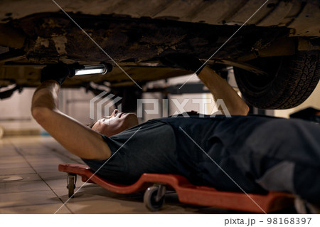 Handsome mechanic guy in uniform overalls is working in auto service with lamp. 98168397