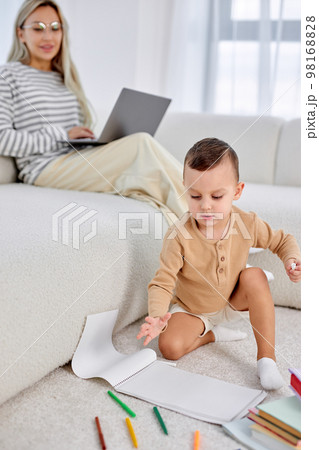 Kid boy and charming mother spending weekends at home together, child drawing on floor 98168828