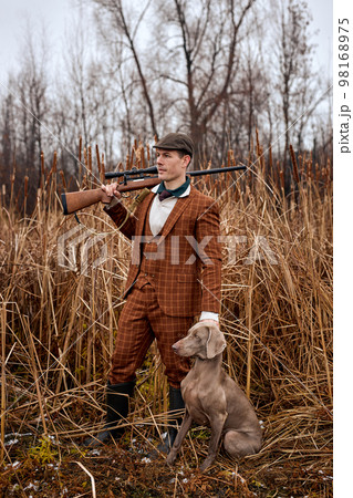 shikari with gray hunting dog in autumn forest. Image taken during big game hunting trip. shikari with gray hunting dog in autumn forest. Image taken during big game hunting trip. 98168975