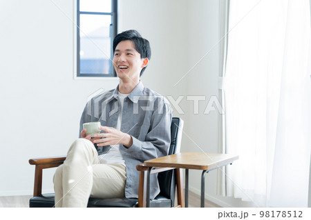 家でコーヒーを飲んでリラックスする若い男性 98178512