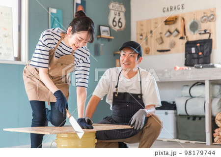 家の倉庫でノコギリで木を切るアジア人男女（DIY教室・ワークショップ・日曜大工・体験教室） 98179744