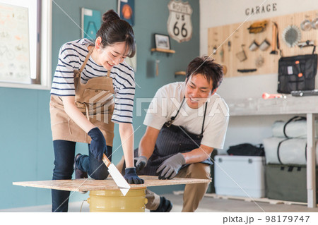 家の倉庫でノコギリで木を切るアジア人男女(DIY教室・ワークショップ・日曜大工・体験教室) 家の倉庫でノコギリで木を切るアジア人男女(DIY教室・ワークショップ・日曜大工・体験教室) 98179747