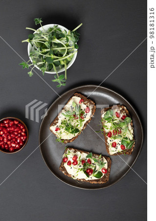 Grain hub sandwiches with soft cheese, microgreens and pomegranate seeds. Top view on a black background Grain hub sandwiches with soft cheese, microgreens and pomegranate seeds. Top view on a black background 98181316