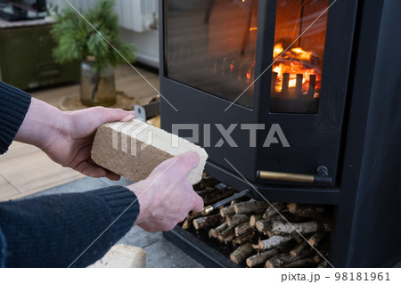 Hands kindle the hearth with economical briquettes. Fuel briquettes made of pressed sawdust for kindling the furnace - economical alternative eco-friendly fuel for the fireplace in the house. Hands kindle the hearth with economical briquettes. Fuel briquettes made of pressed sawdust for kindling the furnace - economical alternative eco-friendly fuel for the fireplace in the house. 98181961