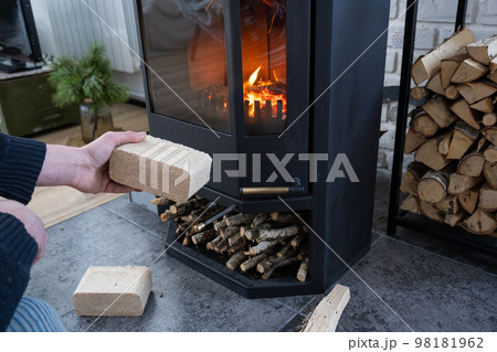 Hands kindle the hearth with economical briquettes. Fuel briquettes made of pressed sawdust for kindling the furnace - economical alternative eco-friendly fuel for the fireplace in the house. Hands kindle the hearth with economical briquettes. Fuel briquettes made of pressed sawdust for kindling the furnace - economical alternative eco-friendly fuel for the fireplace in the house. 98181962