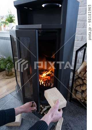 Hands kindle the hearth with economical briquettes. Fuel briquettes made of pressed sawdust for kindling the furnace - economical alternative eco-friendly fuel for the fireplace in the house. 98181965