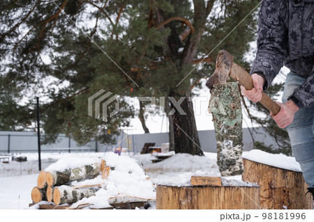 A man is chopping firewood with an axe in winter outdoor in the snow. Alternative heating, wood harvesting, energy crisis 98181996